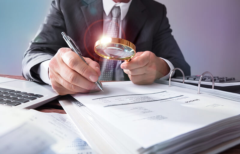 Businessman examining documents with magnifying glass