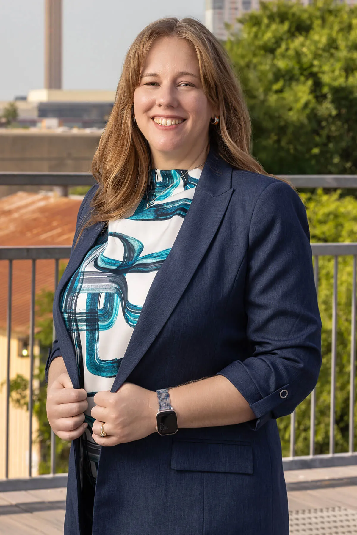 Person in blazer outdoors, smiling.