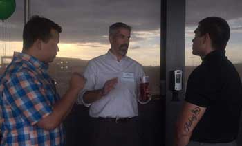 Three people conversing indoors at sunset.
