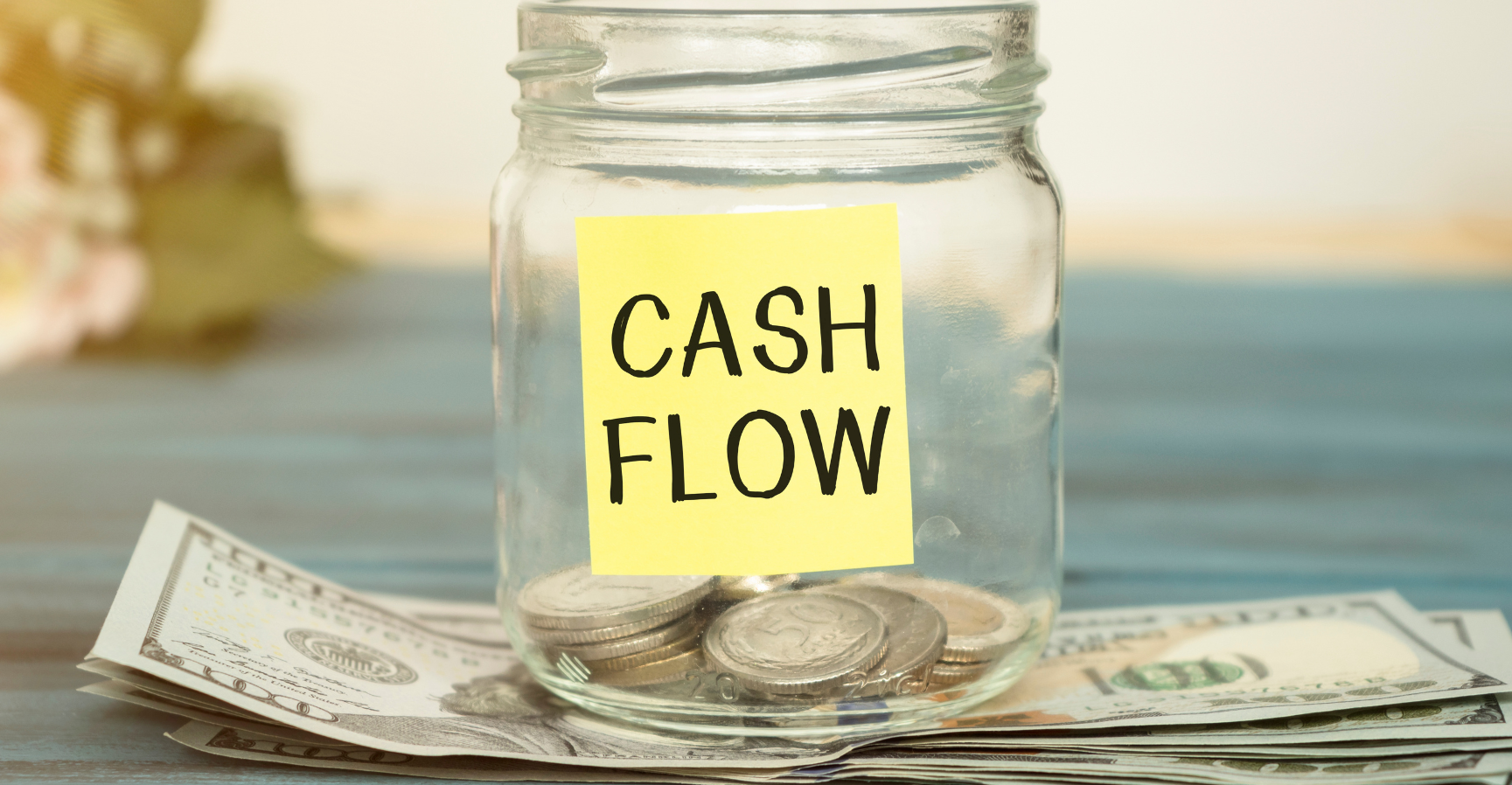 Glass jar with change in it on a table. Sticky note on jar that says cash flow